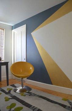 a yellow chair sitting on top of a wooden floor next to a wall painted in blue and gold