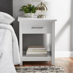 a nightstand with two books and a lamp on it in a bedroom next to a bed