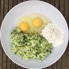 two eggs are sitting on top of shredded green vegetables in a white bowl with flour