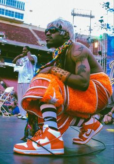 a man in an orange outfit and sneakers on stage with other people watching him from the stands