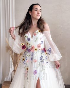 a woman wearing a white dress with flowers on it and a slit through the skirt