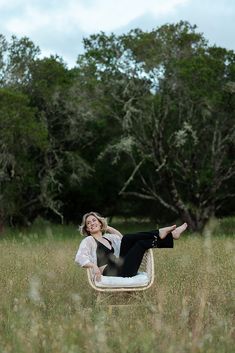 a woman sitting on top of a chair in the middle of a grass covered field