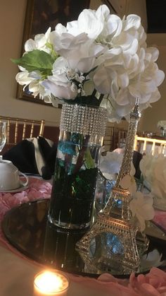 the table is set with white flowers and wine glasses on it, along with an eiffel tower candle holder