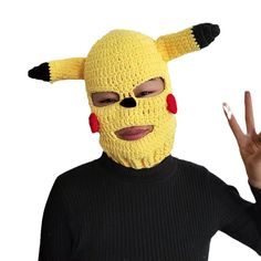 a woman wearing a yellow knitted mask with horns and eyes, making the peace sign