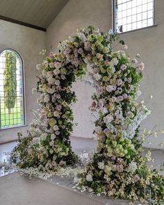 an arch made out of flowers and greenery in front of two stained glass windows