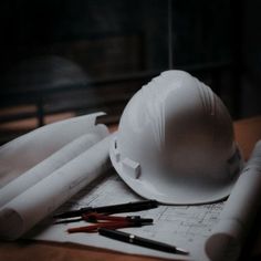 a hard hat sitting on top of construction plans and other tools next to some pens