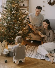 a man and woman sitting on a couch next to a small child near a christmas tree