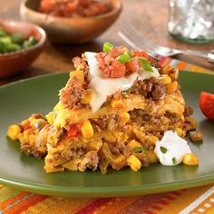 a piece of mexican casserole on a green plate with sour cream and tomatoes