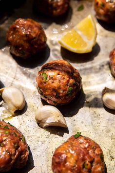 some meatballs and clams are sitting on a baking sheet with lemon wedges