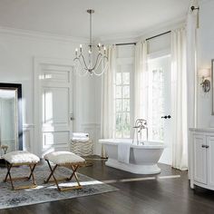 a white bathroom with a chandelier and two stools in front of the tub