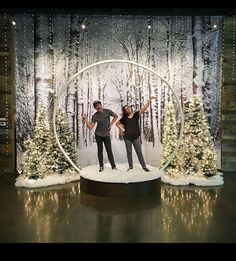 two people are standing in front of a display with christmas trees and snow on the ground