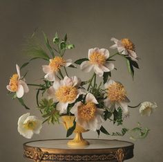 a vase filled with lots of flowers on top of a wooden table in front of a gray wall