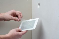 two hands holding a piece of plastic over a hole in the wall