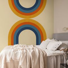 a room with a bed, pillows and a painting on the wall behind it that has a rainbow design