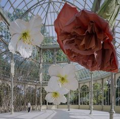 three paper flowers hanging from the ceiling in a glass walled room with people walking by