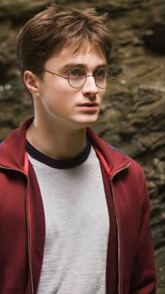 a young man wearing glasses standing in front of rocks