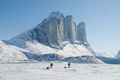 two people are standing in the snow near mountains