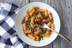 a white bowl filled with pasta and meat on top of a checkered table cloth