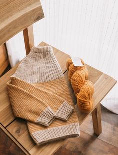 a knitted sweater sitting on top of a wooden chair next to a ball of yarn