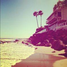 the beach has waves coming in to shore and palm trees on the hill behind it