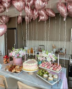 a table topped with lots of cakes and desserts next to balloons hanging from the ceiling