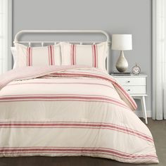 a bed with red and white striped comforter on top of it next to a night stand