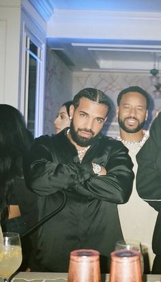 three men standing next to each other at a table with drinks in front of them