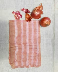 an onion and garlic are sitting on a pink towel next to two onions that have been peeled