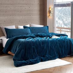 a bed with blue comforter and pillows in a bedroom next to a large window