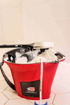 a red bucket filled with cleaning supplies on top of a white tiled floor