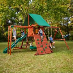 children playing on a wooden swing set in the grass with trees behind them and green roof