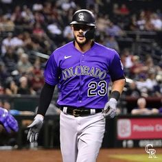 a baseball player walking on the field with his bat in hand and people watching from the stands behind him