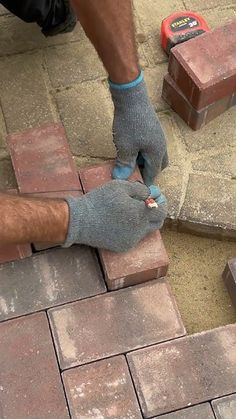 a man laying bricks on the ground with one hand and two other hands in gloves