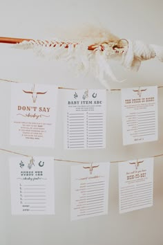 wedding seating cards hanging from a rope in front of a white wall with feathers on it