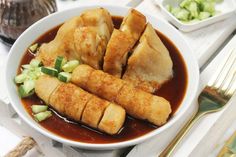 some food is in a white bowl on a table with silverware and utensils