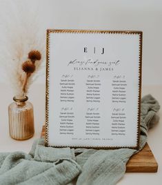 a wedding seating chart on a wooden stand next to a vase with dried pamy plants