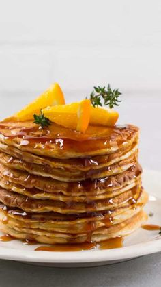 a stack of pancakes with syrup and orange slices on top, sitting on a white plate