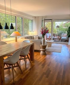 a living room filled with furniture and a wooden table surrounded by white chairs next to a large window