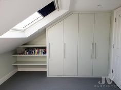 an attic bedroom with white cupboards and bookshelves, skylight and slanted ceiling