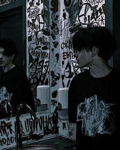 two young men standing in front of a bathroom sink with graffiti on the wall behind them