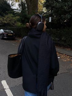 a woman walking down the street with headphones on her ears, wearing a black jacket