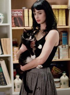 a woman holding a black and white cat in front of a book shelf filled with books