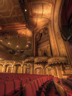 an empty theater with red seats and gold ceilinging is seen in this image taken from the front row