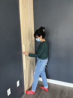 a woman wearing a face mask while standing in front of a tall wooden column with her hands on the wall