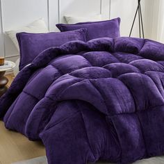 a bed with purple comforter and pillows on it