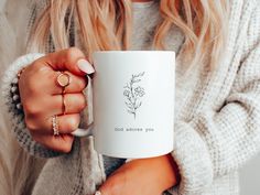 a woman holding a white coffee mug with a flower on it