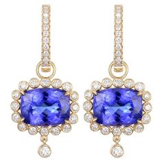 These are resplendent 18-karat yellow gold earrings, each adorned with a central tanzanite stone totaling 5.68 carats. The tanzanites are cut into cushion shapes, their faceted surfaces revealing a deep and enthralling violet-blue hue that tanzanite is renowned for. These stones command attention, their rich color a symbol of sophistication and poise. Surrounding the tanzanite, a halo of round-cut diamonds totaling 0.63 carats adds a dazzling brilliance. The diamonds are precisely set to create a radiant frame around the central stones, their sparkling light enhancing the intense color of the tanzanite. The earrings feature a drop design with a diamond-encrusted bar leading down to the main tanzanite feature. At the end of each earring dangles a single, bezel-set diamond, an elegant finish Tanzanite Diamond Earrings, Cushion Shapes, Tanzanite Stone, Tanzanite Diamond, Yellow Gold Earrings, Drop Design, Bezel Set Diamond, Radiant Diamond