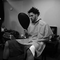 a man with dreadlocks sitting in a chair holding a mirror and looking at his reflection