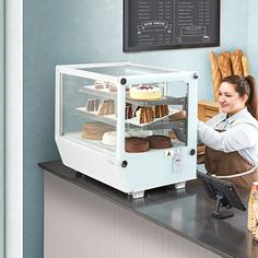 a woman standing in front of a display case filled with cakes and pastries,