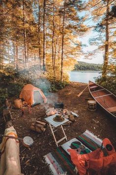 there is a tent and campfire in the woods next to some boats on the water